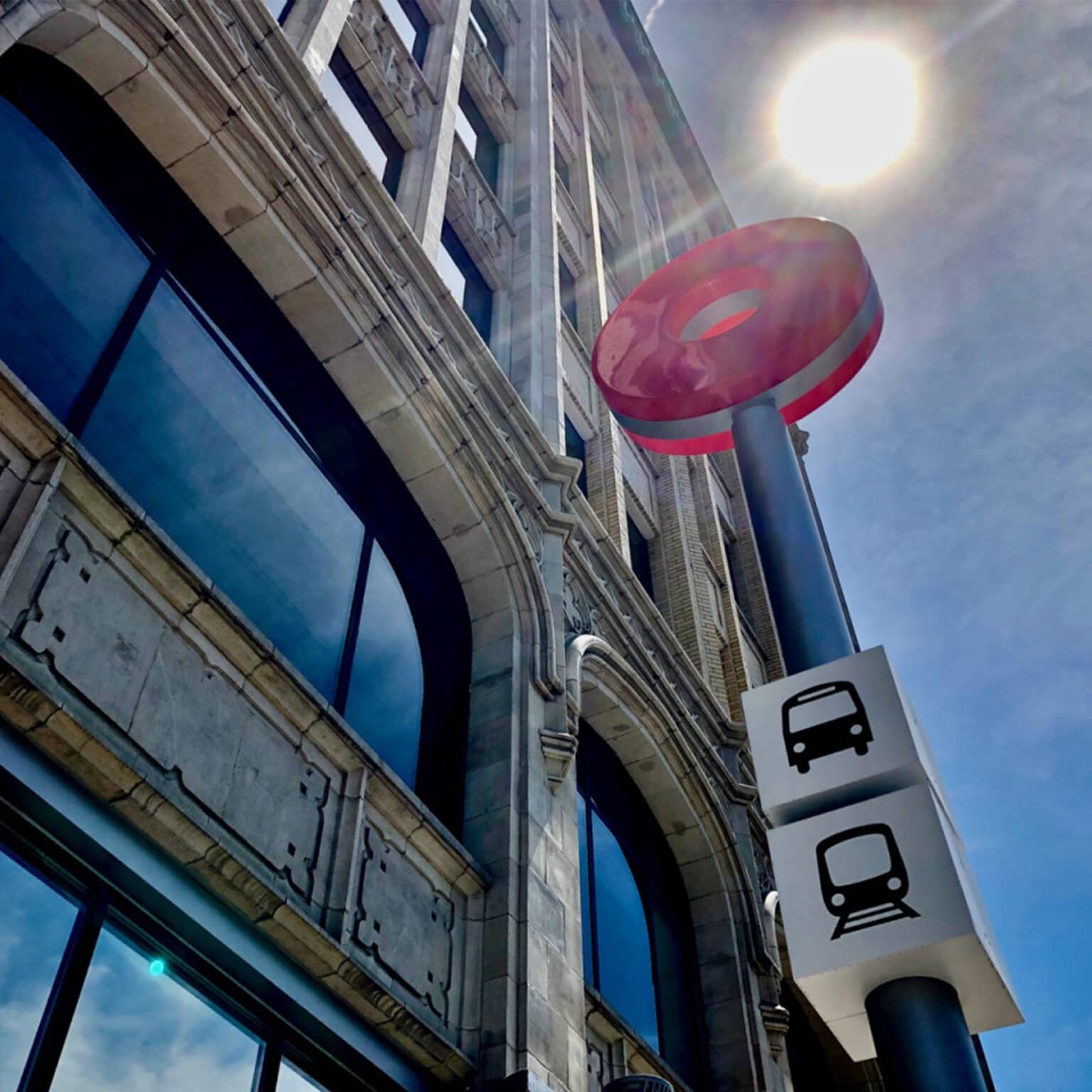 Looking upward at sign topped with the system identifier, a brightly shining sun in the background.