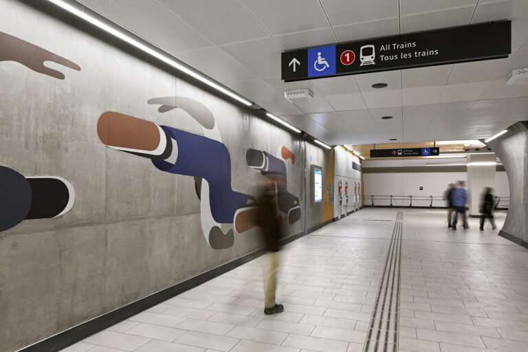 Overhead directional sign adjacent to a wall mural in an OC Transpo station.