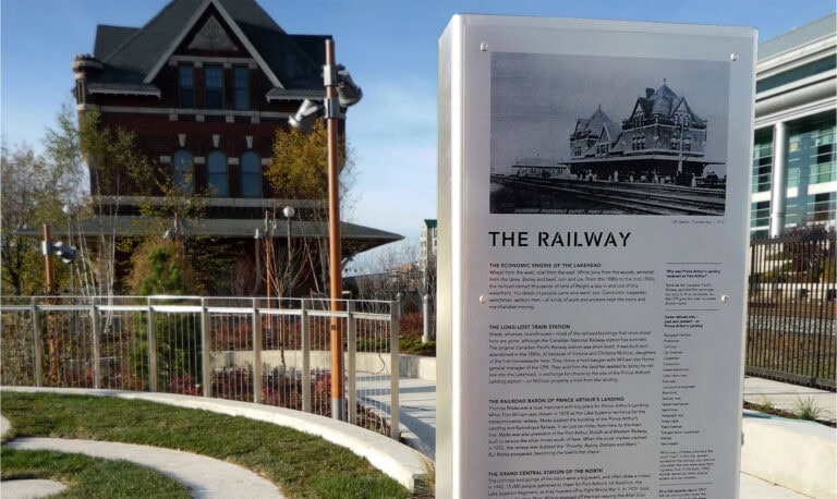 Prince Arthur's Landing interpretive sign on "the railway" infront of heritage building.