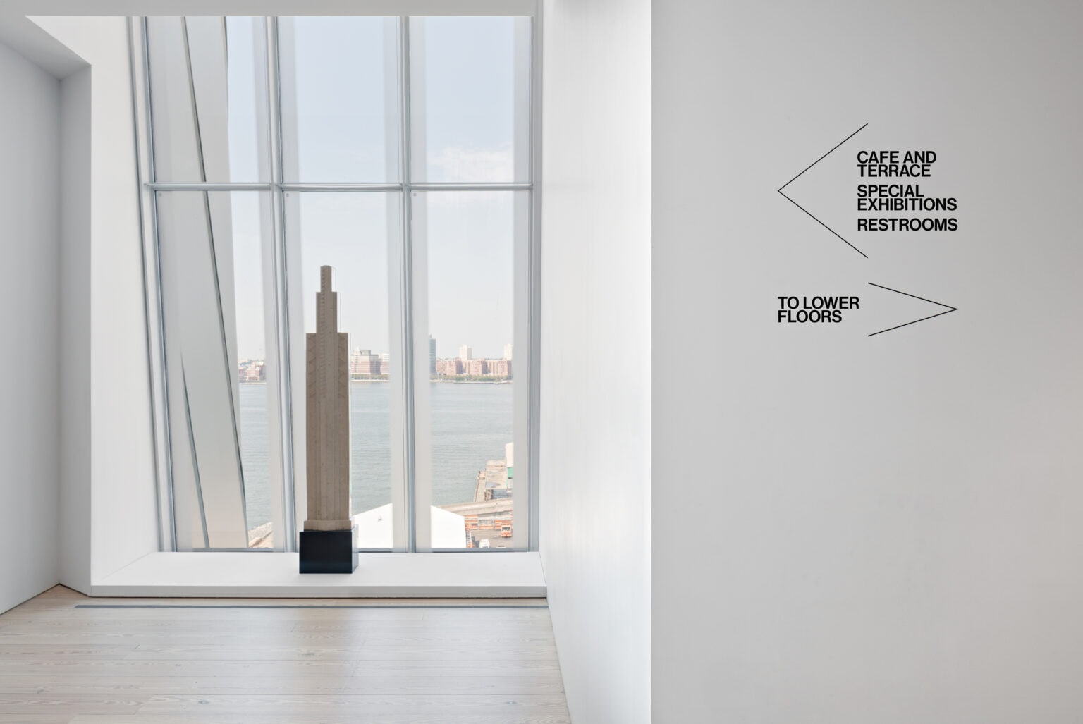 Whitney Museum white, minimalist gallery space, with minimalist wayfinding signage applied directly to white wall.