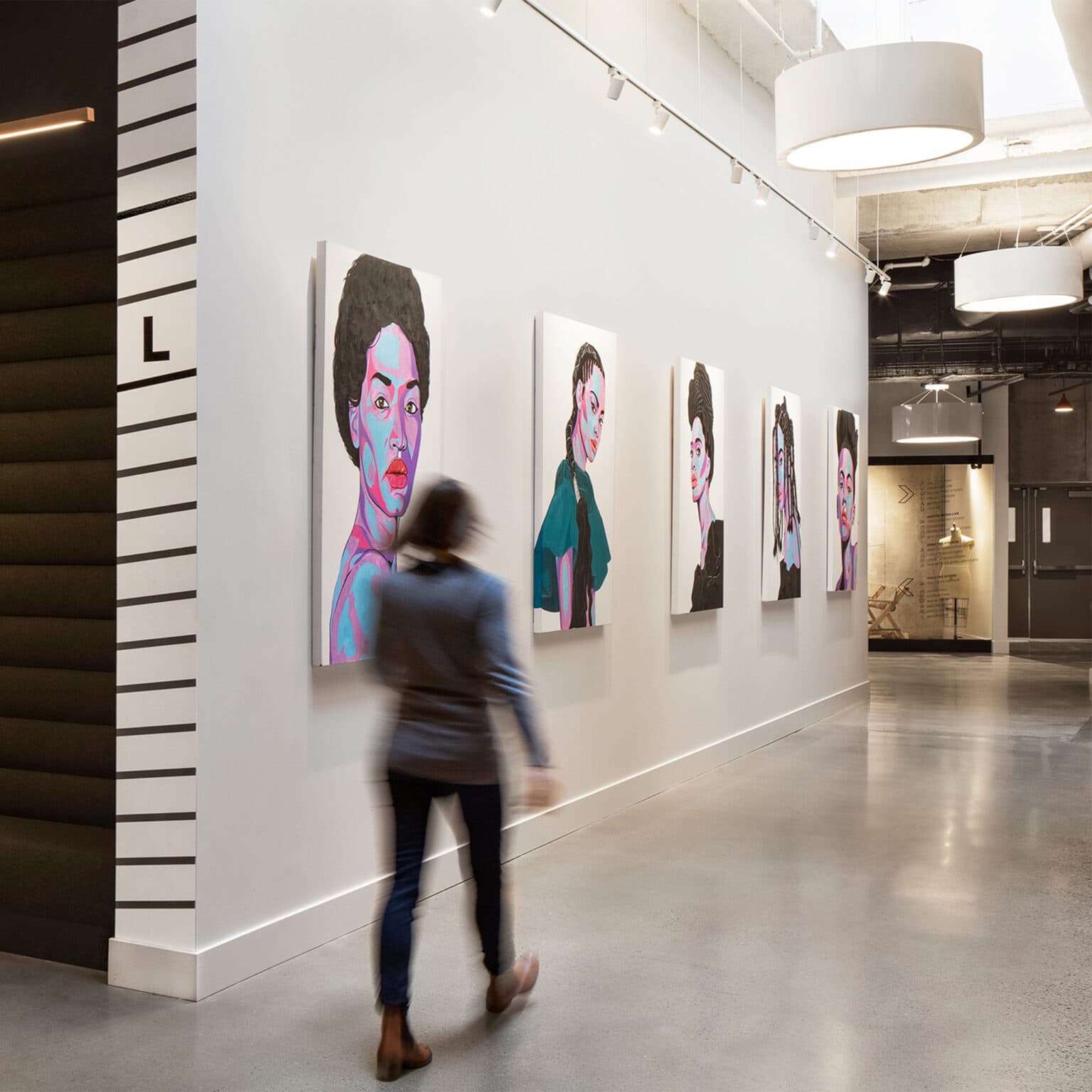 Corridor with artwork in the form of stylized portraits alongside area identification signage featuring angled lines.